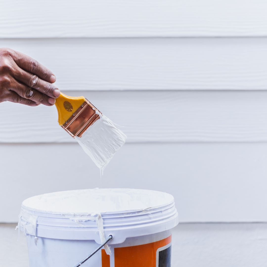 paint brush with white paint on it being held over a bucket