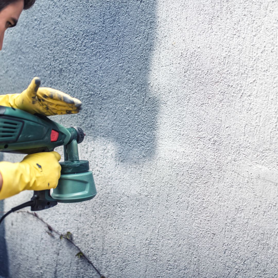 man using paint sprayer to paint a house